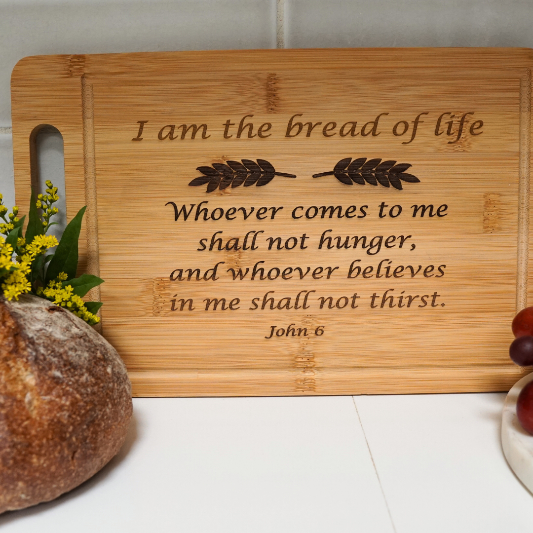 Bread board with engraved scripture "I am the bread of life" with bread and grapes on counter