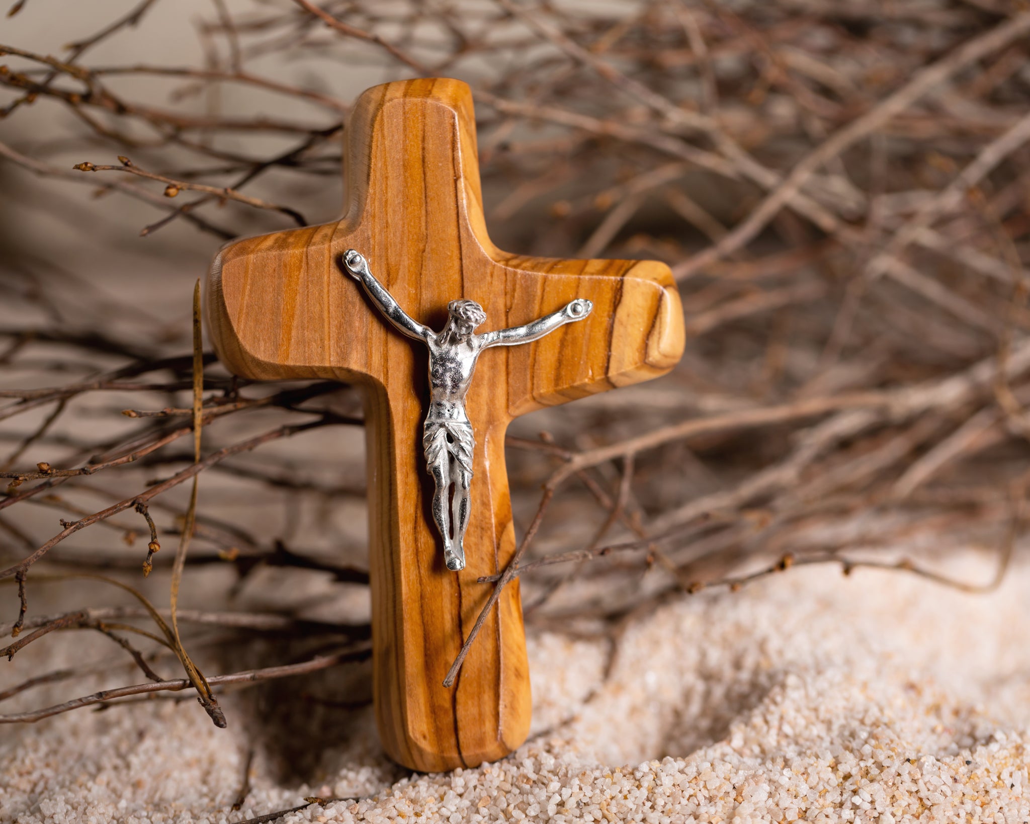 Olive wood crucifix in sand with branches