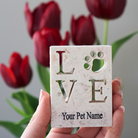 Hand holding personalized stone plaque with LOVE and a paw print with red tulips in the background