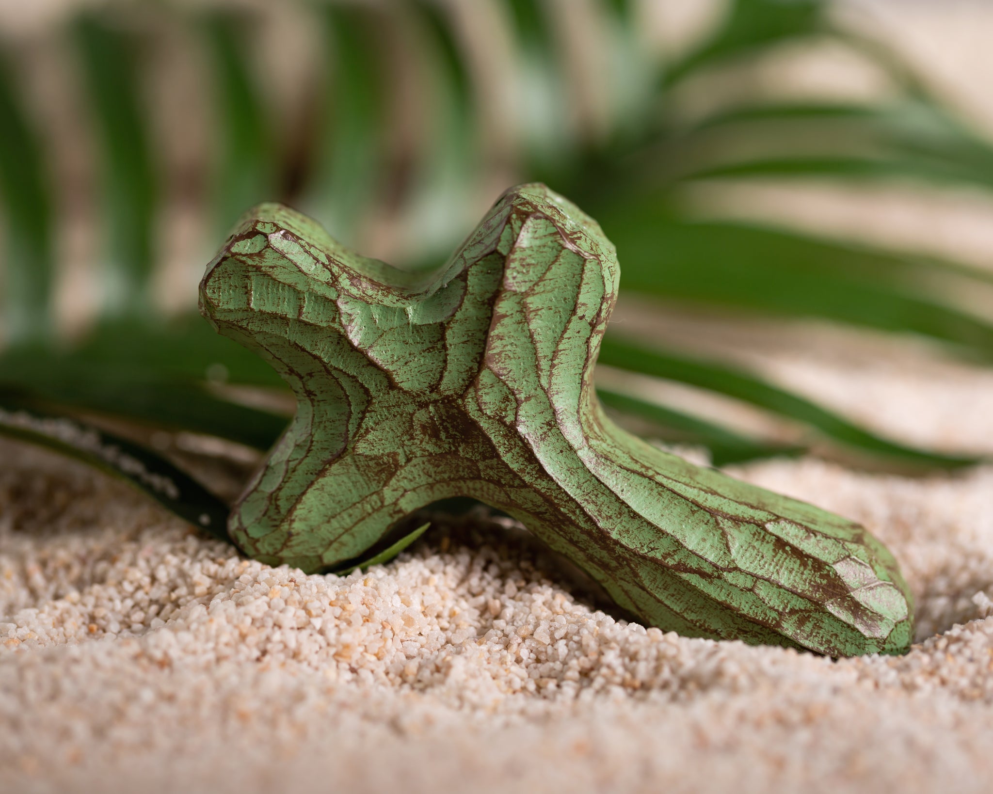 Green painted holding cross in sand with palm leaves